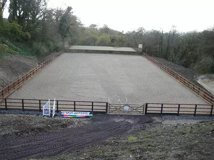 A completed outdoor equestrian arena by Total Equestrian Construction, featuring a level sand surface, secure timber fencing, and jump equipment ready for training or competition.