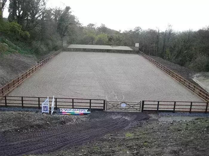 A completed outdoor equestrian arena by Total Equestrian Construction, featuring a level sand surface, secure timber fencing, and jump equipment ready for training or competition.