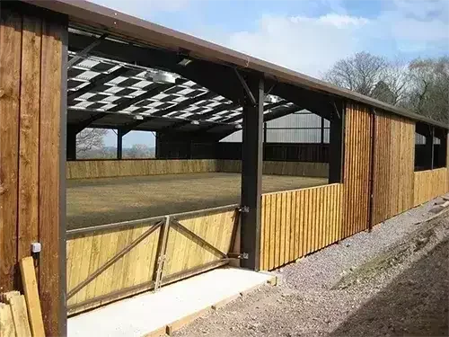 An indoor equestrian arena with timber cladding, skylights, and wooden kickboards around the riding area.