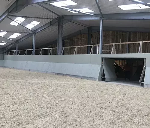 This image shows an indoor equestrian arena with steel framework and timber panels, built as a durable structure for long-lasting performance.