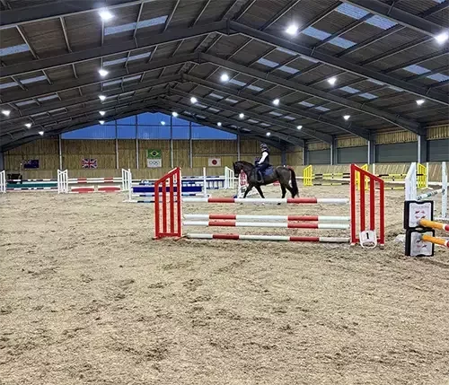 This image shows an indoor equestrian arena with a sand surface and strong steel frame, designed with tailored layouts for dressage, jumping, and multi-discipline training.
