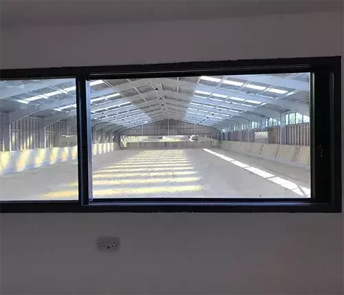 This image shows an indoor equestrian arena viewed through a large window, demonstrating the option of integrated viewing galleries for spectators and trainers.