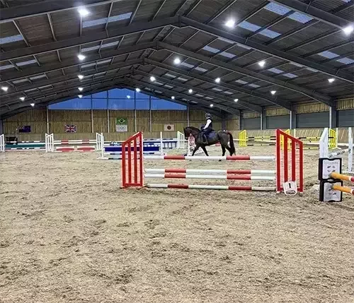This image shows an indoor equestrian arena with a sand surface and strong steel frame, designed with tailored layouts for dressage, jumping, and multi-discipline training.