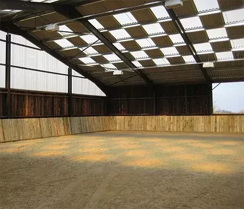This image shows an indoor equestrian arena with timber kickboards and a roof engineered for precision ventilation and natural light design.