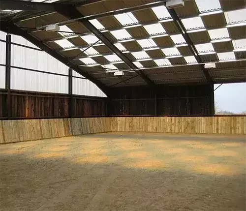 This image shows an indoor equestrian arena with timber kickboards and a roof engineered for precision ventilation and natural light design.