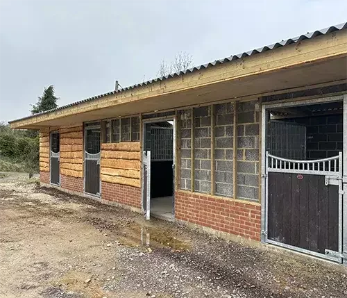 This image shows a part-built stable block with brick, timber, and steel finishes, designed with tailored stable layouts to suit your yard and individual needs.