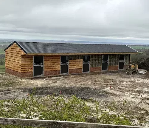 This image shows a newly built stable block with timber and brick finishes, where thoughtful landscaping around the stables enhances drainage, access, and the overall yard setting.